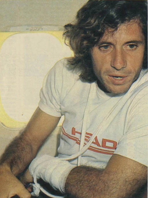 Guillermo Vilas seated inside an aircraft, wearing a white shirt, looking toward the camera.