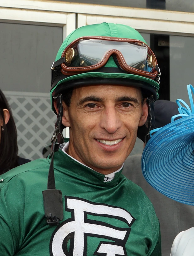 Johnny Velazquez in racing silks and helmet, smiling at the track.