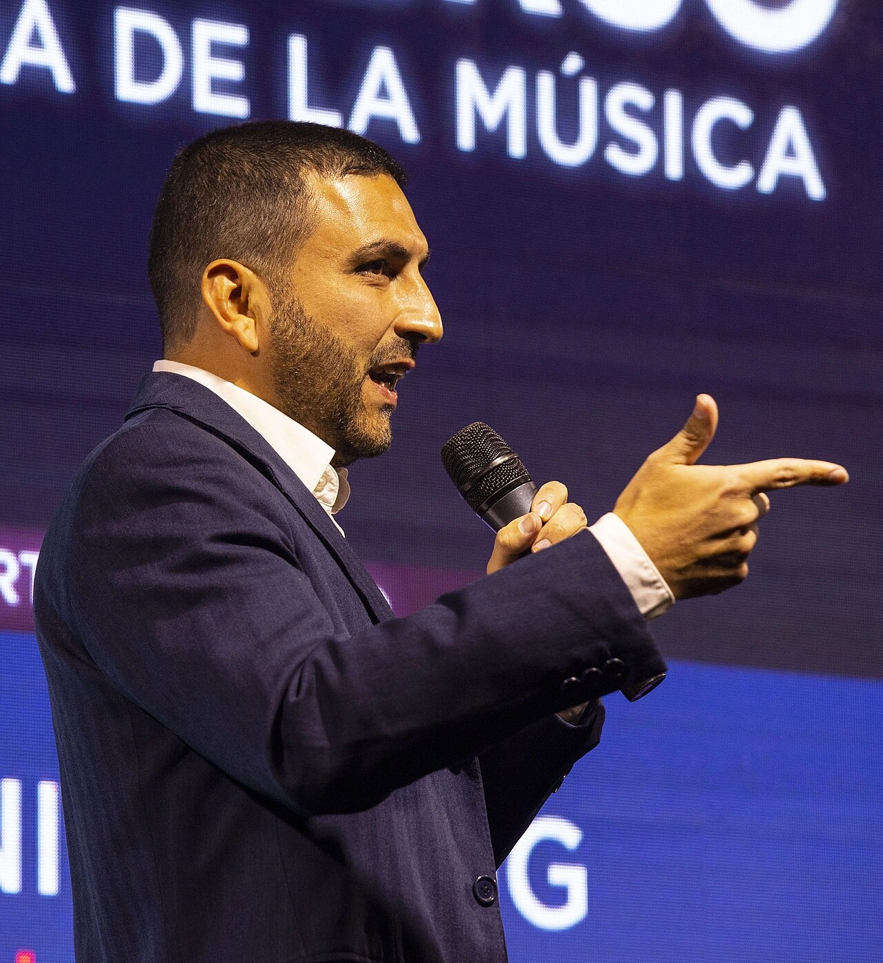 Vicente Saavedra speaking on stage with a microphone at a music event